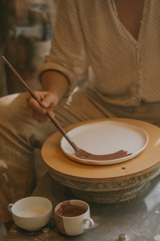 An artisan carefully paints a ceramic plate in a cozy workshop, embodying craftsmanship and creativity.